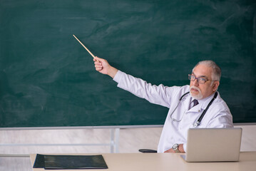 Old male doctor teacher in front of blackboard