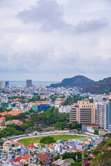 Fototapeta premium Panoramic coastal Vung Tau view from above, with waves, coastline, streets, coconut trees and Tao Phung mountain in Vietnam.