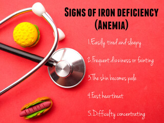 Stethoscope and western food toys with text Signs of iron deficiency (ANEMIA) on a red...