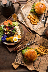 Two homemade beef burgers with potato fries and fruit and vegetable salad old wooden table background board in a rustic. Side view, Close up,Selective focus.