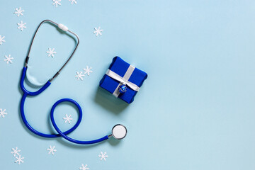 Merry Christmas and Happy New Year medicine concept, blue stethoscope, snowflakes, small gift box present. Winter holiday background