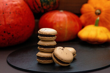 Dessert for Halloween. Thanksgiving menu. French macarons. Macaroons with chocolate on a black background with pumpkins. Soft selective focus.