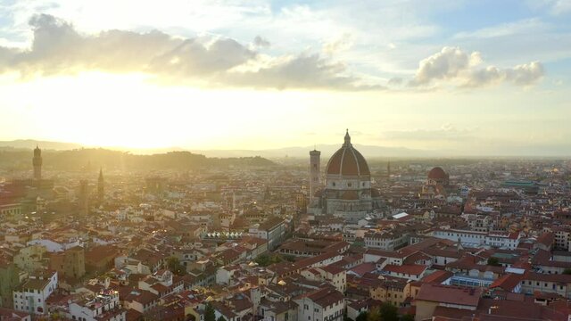 Florence, Tuscany, Italy, October 2021. Drone tracks parallel with the Cathedral of Santa Maria del Fiore from the east with the Palazzo Vecchio in the foreground at sunset.