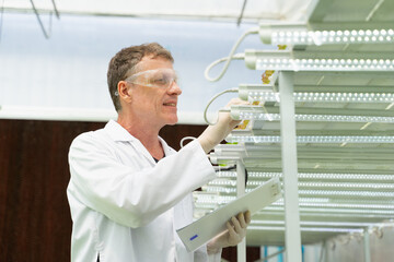 Caucasian male botanist, geneticist, or scientist in white coat and eyeglasses holding clipboard...