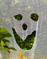 Ghost face of white cloth on background of green autumn park on Halloween party