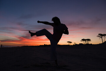 silueta de hombre practicando artes marciales al atardecer en la playa