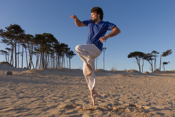 joven practicando artes marciales al atardecer sobre dunas de arena, saltando 