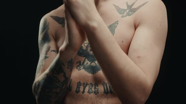 Portrait of brutal naked man, having earrings in nose and ears, strong muscle guy posing, rubbing hands together near face, thinking, worried about the fight, looking in camera with serious view. 