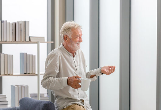Senior man inside new home during a coffee break, Elderly man standing near window with cups of coffee