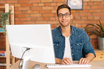 Portrait of confident cheerful handsome young freelance designer male in stylish glasses working on...