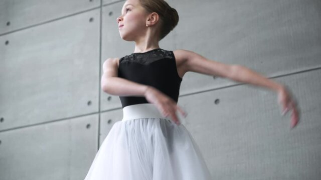 Elegant little girl in a black and white tutu dress, dance ballet and perform choreographic elements on a gray background, rehearsal.