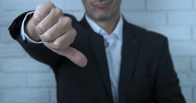 Show failure in man business. A businessman with problems in business show his thumb down in the office.