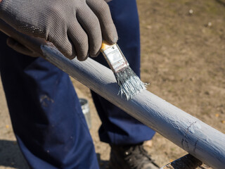 Person paints pipe with primer outdoors. Close up hand in gloves which hold yellow brush and cover...