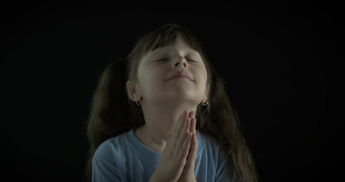 A child at prayer. Little girl prays in the dark.