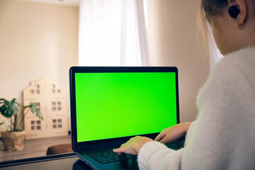 A young girl works on a laptop screen chromakey typing text at home at the workplace in a bright room.