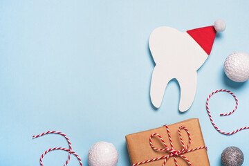 Christmas and New Year background for dentistry. Decorative model tooth in a red Santa Claus hat, gift and festive decoration. Creative medical winter greeting card. Top view, copy space, flat lay