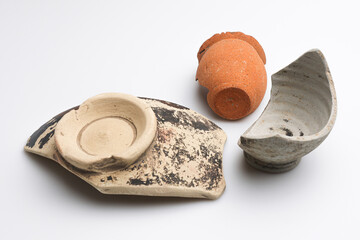 Archeologia: frammenti di vasetti e ciotole di epoca romana di vari materiali e colori, isolate su fondo bianco 