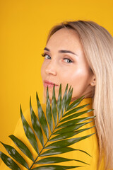 Naklejka premium Beauty portrait of a young, beautiful blonde woman with good skin in yellow clothes holding a green leaf on a yellow background