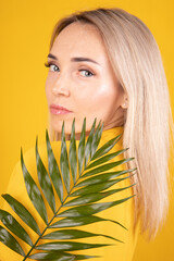 Naklejka premium Beauty portrait of a young, beautiful blonde woman with good skin in yellow clothes holding a green leaf on a yellow background