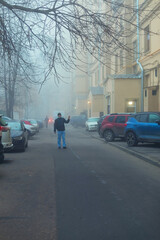 A man in a green protective mask waves his hand in the courtyard of a house, fog behind him. Pandemic. Selective focus. Quarantine. Stay home.