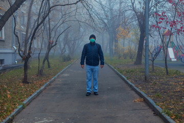 A man in a green protective mask on his face in the yard against a background of fog. Pandemic. Selective focus. Quarantine. Stay home.