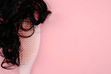Curls or curls of black hair lie on a massager comb on a pink background.Head massage, hair care,...