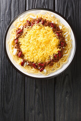 Authentic Cincinnati Chili is a meaty, rich, and uniquely spiced chili served over hot spaghetti with cheese toppings closeup in the plate on the black table. Vertical top view from above