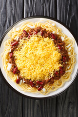 Cincinnati chili or Cincinnati style chili is a Mediterranean spiced meat sauce used as a topping for spaghetti closeup in the plate on the black table. Vertical top view from above