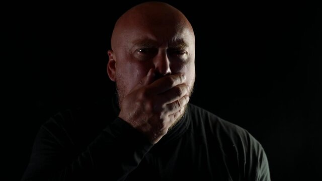 A bald man with a sore throat coughs violently on a black background
