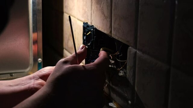 Electrician man repair an electrical outlet socket in apartment in the dark. Static shot. home renovation concept