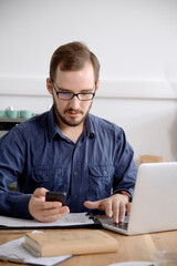 Man using laptop and smart phone while sitting at wooden table