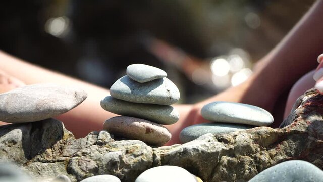 Woman bilds stones pyramid on the seashore on a sunny day on the blue sea background. Happy holidays. Pebble beach, calm sea, travel destination. Concept of happy vacation on the sea, meditation, spa