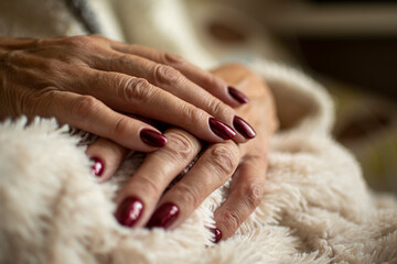 Manicure closeup and dark red nails. Cozy indoor concept, elegant colors, luxury treatment. Female hand closeup. Selective focus on the details, blurred background.