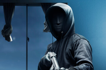 Criminal man in a hidden mask holding the shotgun while robbery the house