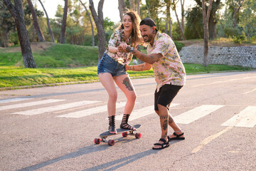 Young cool tattooed man teaching his girfriend how to skateboarding.
