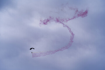 Parachutist with red smoke at Axalp Canton Bern air show of Swiss Air Force on a cloudy grey autumn day. Photo taken October 19th, 2021, Brienz, Switzerland.