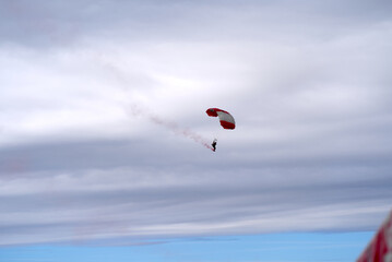 Parachutist with red smoke at Axalp Canton Bern air show of Swiss Air Force on a cloudy grey autumn day. Photo taken October 19th, 2021, Brienz, Switzerland.
