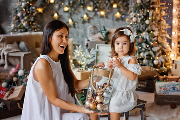 Mother and daughter are looking at Christmas decorations gold, silver and brown Christmas balls. They take it out of a large glass jar.