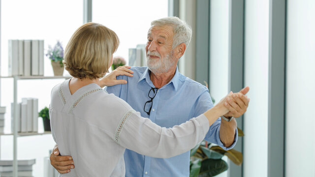 Caucasian Old Senior Elderly Happy Lovely Lover Grandparent Marriage Couple Listening To Slow Waltz Rhythm Music Holding Hands Smiling Embracing Hugging Cuddling Tenderness Dancing Together At Home