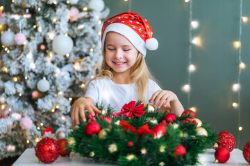 Santa little helper with decorative christmas tree on background. Little smiling girl make...
