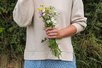 A girl in a white blouse holding wildflowers in her hand in a forest.