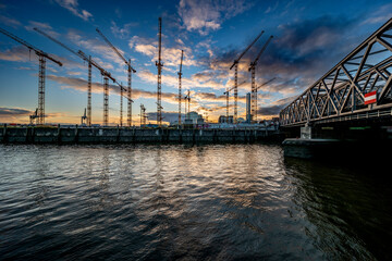 Wide angle view of a construction site with a lot of cranes and a bridge in the HafenCity of Hamburg in the evening