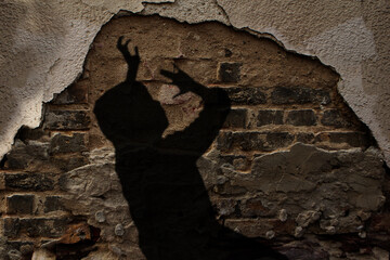blurred black shadow of a child with raised hands in a pleading gesture against background of an old brick wall, the concept of domestic violence, a victim of abuse