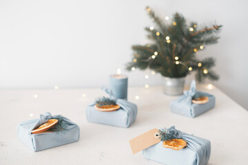 Christmas gift in eco friendly reusable fabric package. Decorated dried orange fruits, fir branches, tag on grey background. Japanese style furoshiki. Top view. Place for text