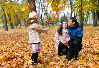 Family portrait in an autumn park. Happy people playing with fallen yellow leaves.