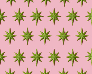 Creative festive pattern made of Christmas green stars on pastel pink background. Minimal New Year idea with ornaments. Aesthetic flat lay.