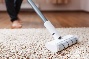 Human legs and a white turbo brush of a cordless vacuum cleaner cleans the carpet in the house