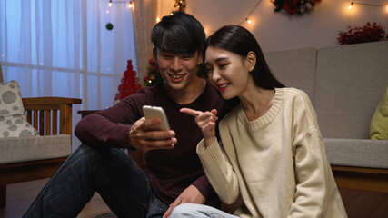 Happy asian couple relaxing enjoy leisure time in living room on carpet by xmas tree at night....