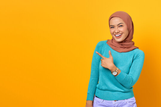 Portrait Of Smiling Young Asian Woman Pointing Finger At Copy Space On Yellow Background