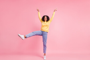 Photo of adorable pretty dark skin girl dressed yellow pullover walking showing v-signs smiling...
